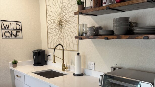 A modern kitchen with white cabinetry, a built-in dishwasher, a coffee maker, and a toaster oven. - Welcome to the Sundancer @ the Little Littleton Village (Littleton)