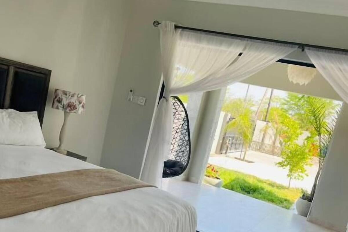 Un dormitorio espacioso con una cama grande, un banco y vistas a un jardín a través de una ventana.