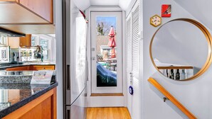 A narrow hallway with a kitchen on one side, a door leading to a balcony, and a round mirror on the wall. - Harbor Views, Parking, Roof Deck, Beach - West End (Provincetown)