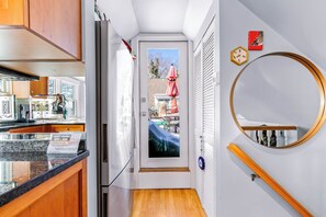 Ein schmaler Flur mit einer Küche an einer Seite, einer Tür, die auf einen Balkon führt, und einem runden Spiegel an der Wand.