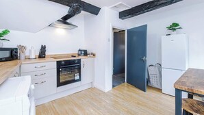 A compact kitchen with white cabinets, a wooden countertop, a built-in oven, and a microwave. There's a dark blue door leading to another room, and a small table with a plant. - Charming Grade II Listed Apartment | Sleeps 4 (Wem)