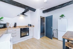 A compact kitchen with white cabinets, a wooden countertop, a built-in oven, and a microwave. There's a dark blue door leading to another room, and a small table with a plant. - Charming Grade II Listed Apartment | Sleeps 4 (Wem)