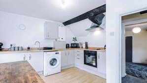 A compact kitchen with a washing machine, oven, microwave, and white cabinets. - Charming Grade II Listed Apartment | Sleeps 4 (Wem)