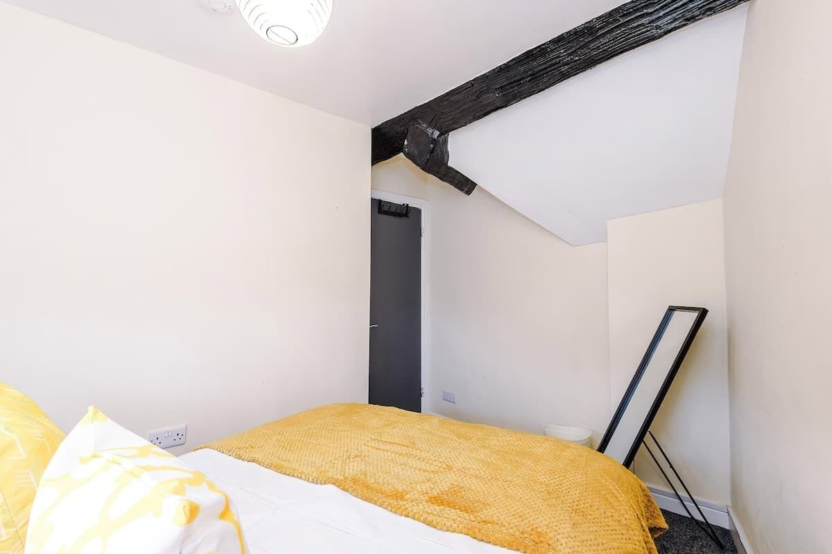 A bedroom with a bed, a door, a mirror, and a ceiling beam.
