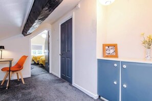 A hallway with a door, a desk with a chair, a cabinet, and a bed in the background. - Charming Grade II Listed Apartment | Sleeps 4 (Wem)