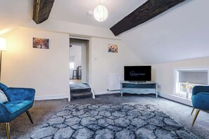 A modern living room with a flat-screen TV, two blue armchairs, a patterned rug, and a staircase leading to another room. - Charming Grade II Listed Apartment | Sleeps 4 (Wem)