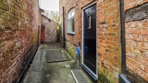 A narrow alleyway with brick walls, a metal grate, and a blue hose. - Charming Grade II Listed Apartment | Sleeps 4 (Wem)