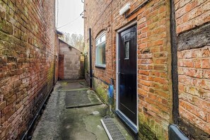 A narrow alleyway with brick walls, a metal grate, and a blue hose. - Charming Grade II Listed Apartment | Sleeps 4 (Wem)