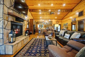 A cozy log cabin interior with a stone fireplace, leather sofas, a dining area, and a kitchen. - Hoot's Hideaway spacious family friendly hot tub (Broken Bow)