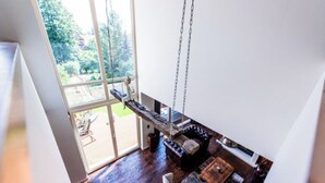 A spacious room with a large window, a wooden swing, and a cozy seating area with a fireplace.