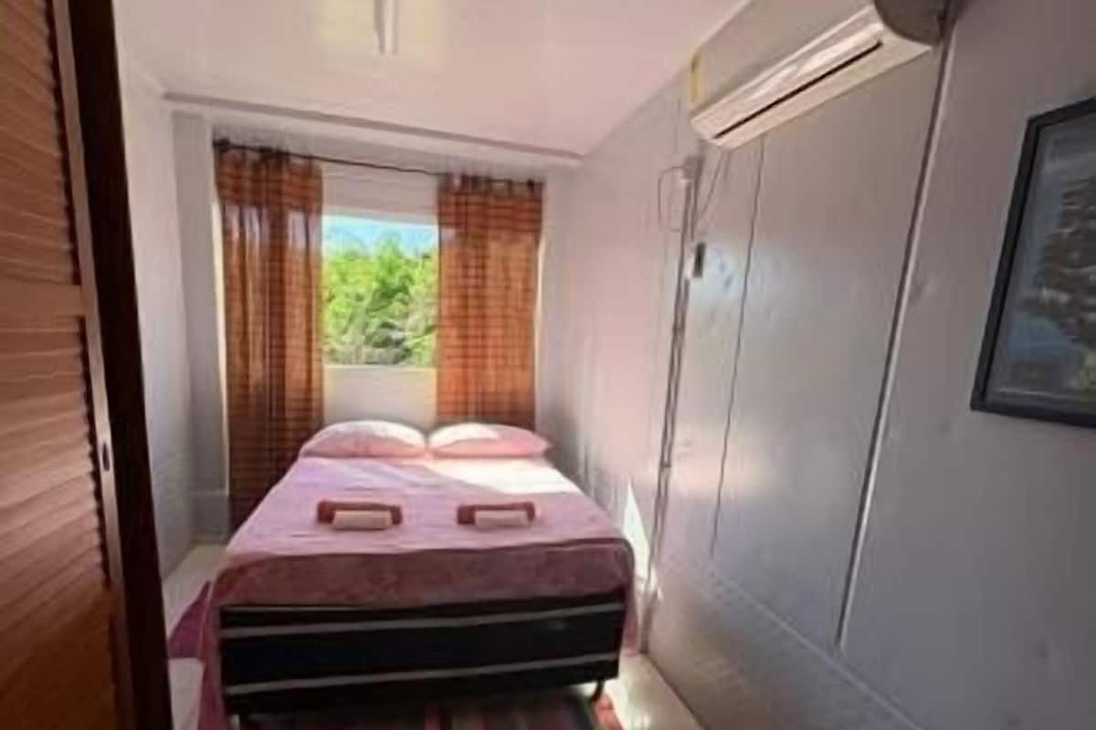 A bedroom with a bed, a window with curtains, and a wall-mounted air conditioner.