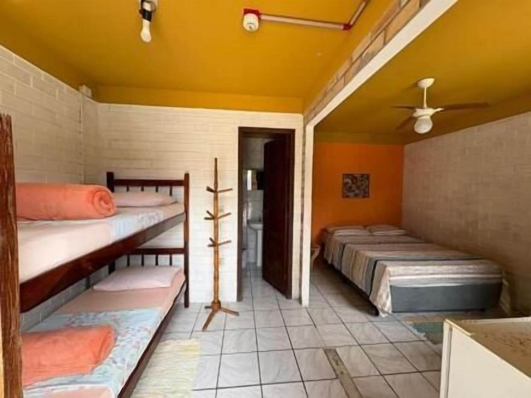 A dormitory room with bunk beds, a standing fan, and a door leading to another room.