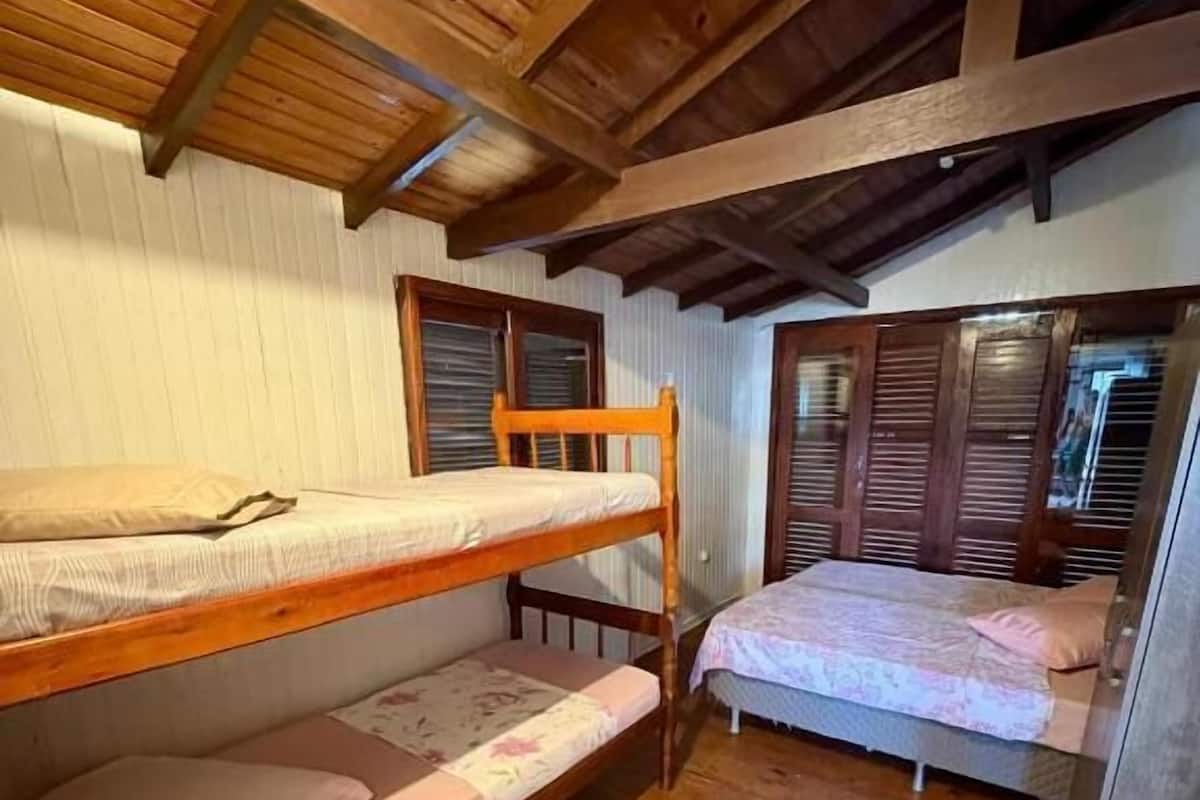 A room with two wooden bunk beds, a small stool, and a window with shutters.