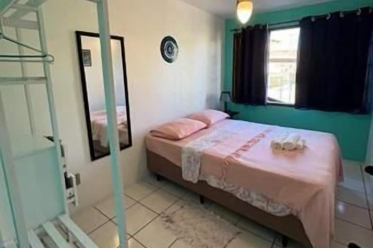 A bedroom with a bed, a ceiling fan, a window with curtains, and a mirror on the wall.