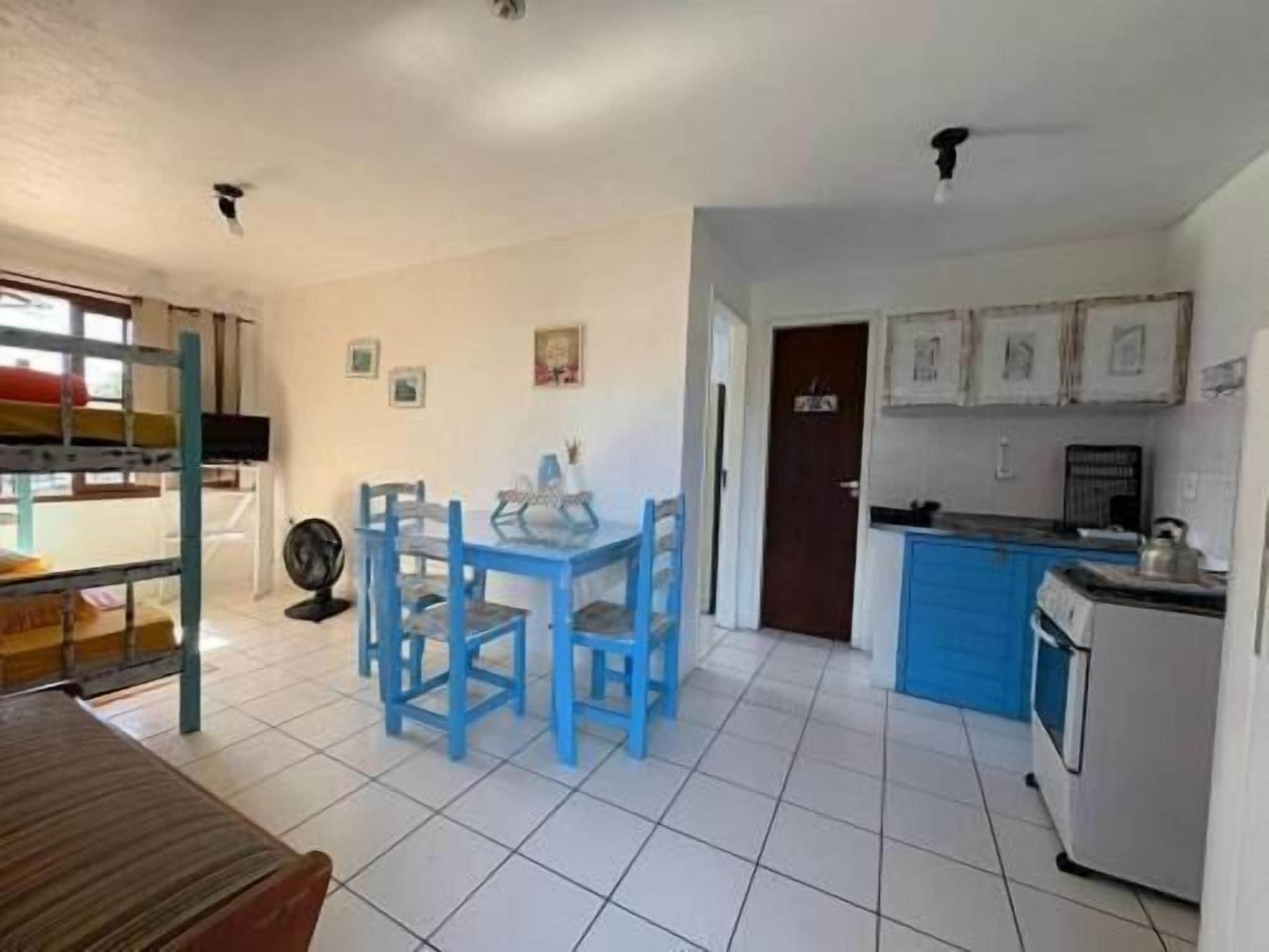 Een compacte keuken met blauwe kastjes, een eettafel met stoelen en een kleine koelkast.