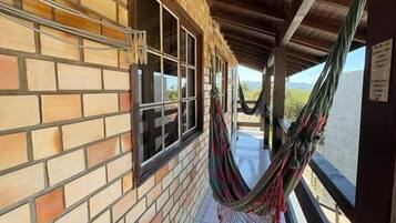 Un espacio al aire libre techado con pared de ladrillo, ventanas y una hamaca.