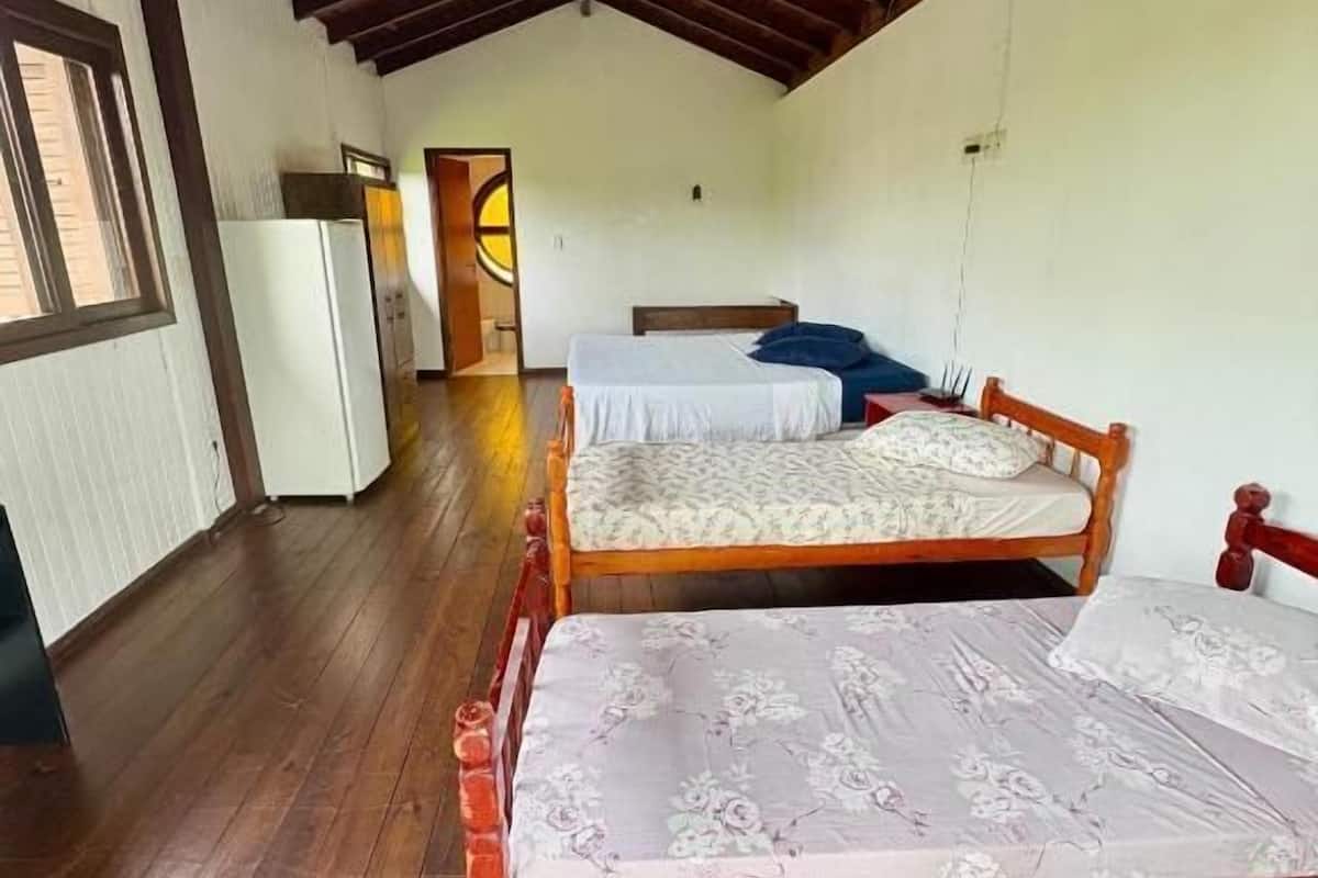 A room with a wooden floor, a bed with a floral bedspread, a wooden headboard, and a window with blinds.