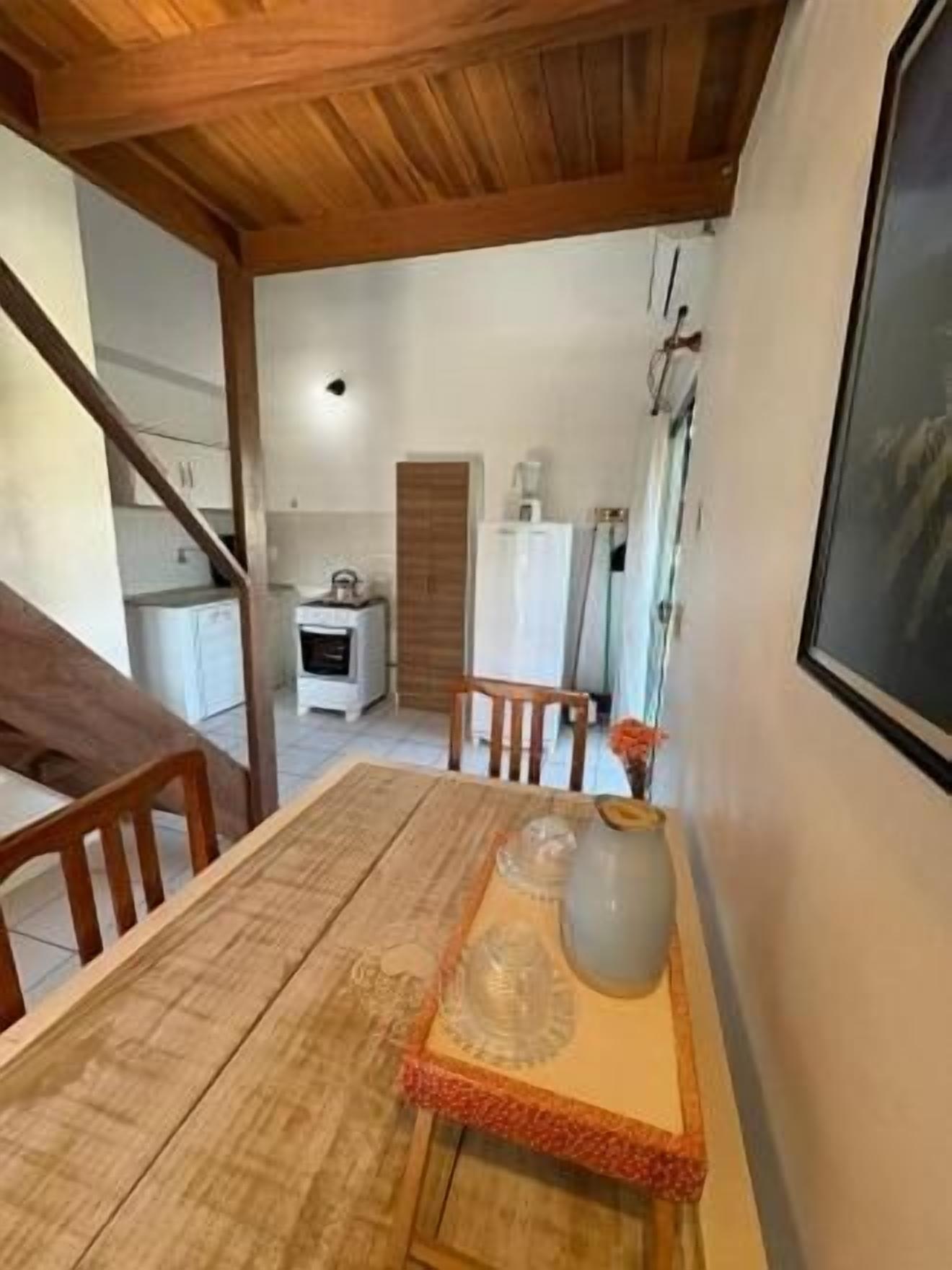 Un comedor con una mesa de madera, sillas y un jarrón. Se ve una cocina al fondo.