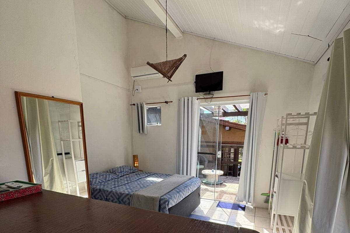 A room with a bed, a table, a mirror, a TV, and a sliding door leading to an outdoor area.