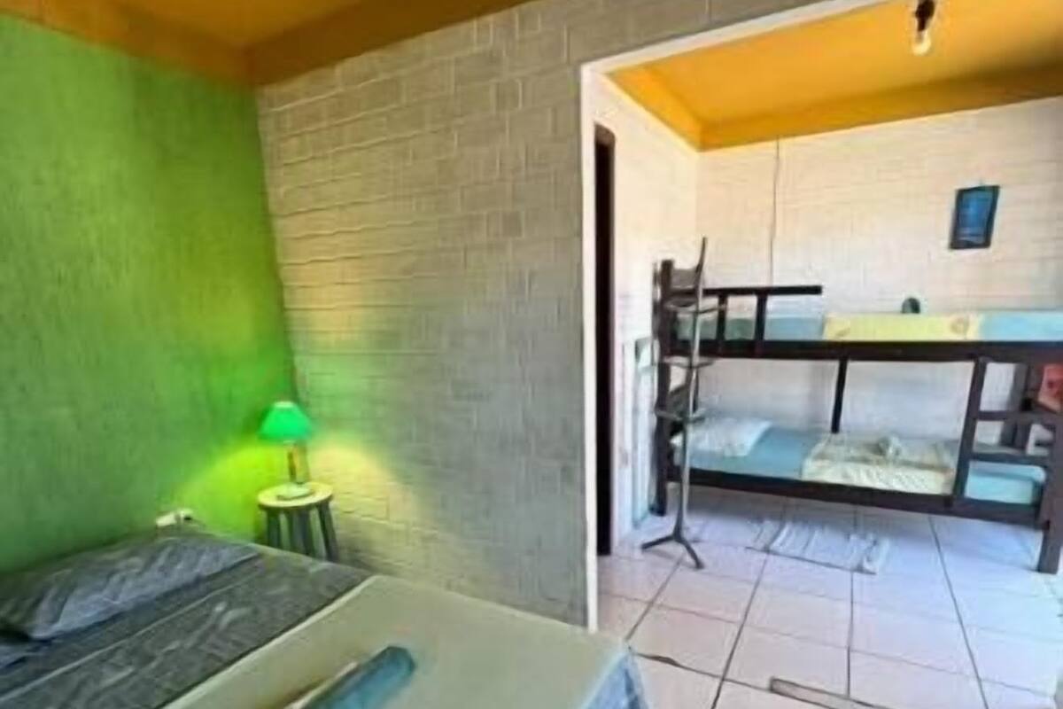 A room with a bunk bed, a green wall, a small table with a lamp, and a tiled floor.