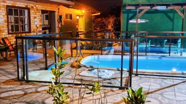 Uma área de piscina com guarda-corpo de vidro, um edifício de tijolos e um letreiro com a palavra 'LAZER'.