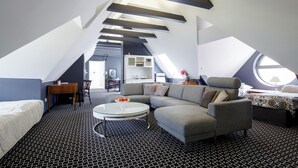 A modern loft bedroom with a sloped ceiling, a gray sectional sofa, a round coffee table, and a large window providing natural light. - Cocorico Boutique Stay Adults Only (Szczecin)