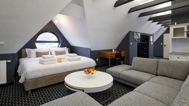 Una habitación moderna y compacta con una cama, una mesa de centro redonda y un sofá.