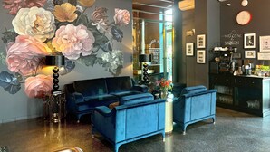 A reception area with a blue sofa, a coffee station, and a wall mural of flowers. - Cocorico Boutique Stay Adults Only (Szczecin)