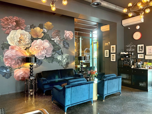 A reception area with a blue sofa, a coffee station, and a wall mural of flowers.