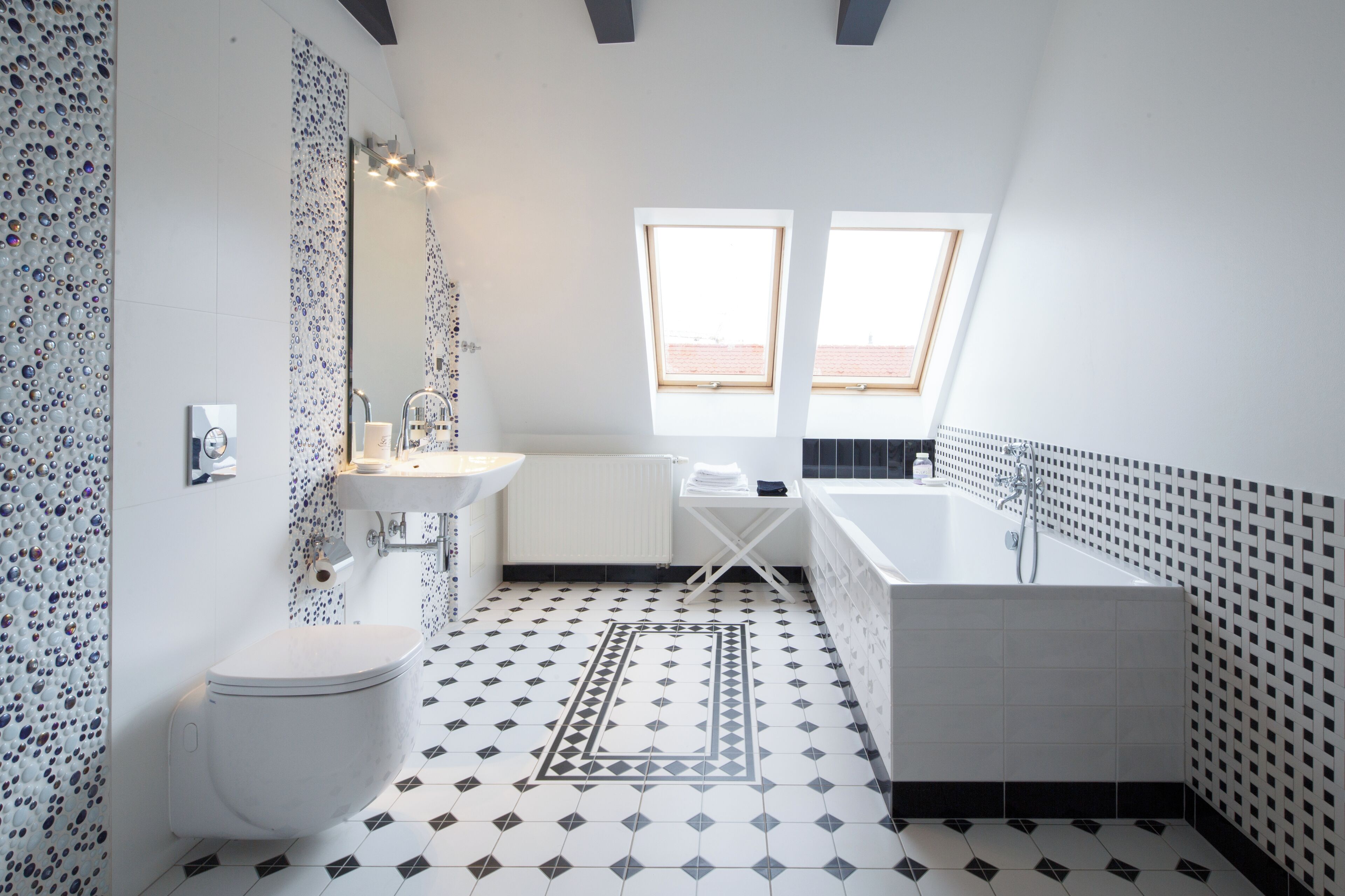 A modern bathroom with a white toilet, a sink, a bathtub, and a shower. There are two windows providing natural light and a decorative rug on the floor.