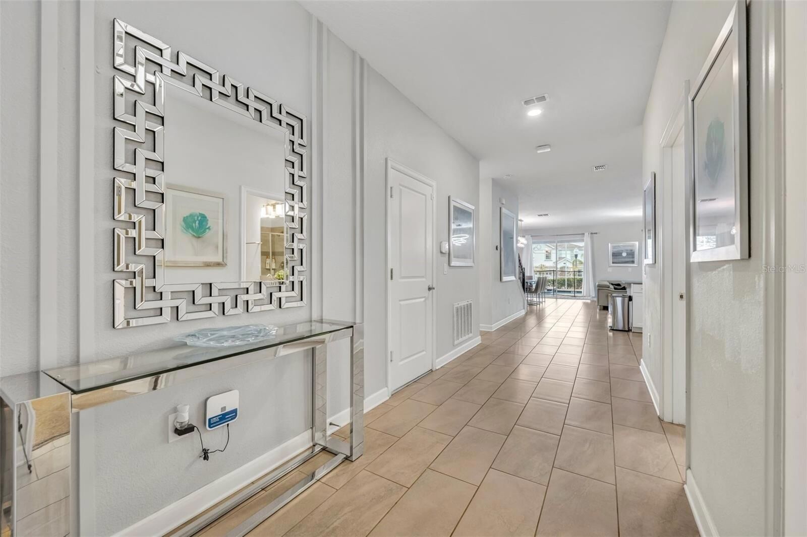 A modern hallway with a glass console table, a geometric mirror, and a view to a balcony.