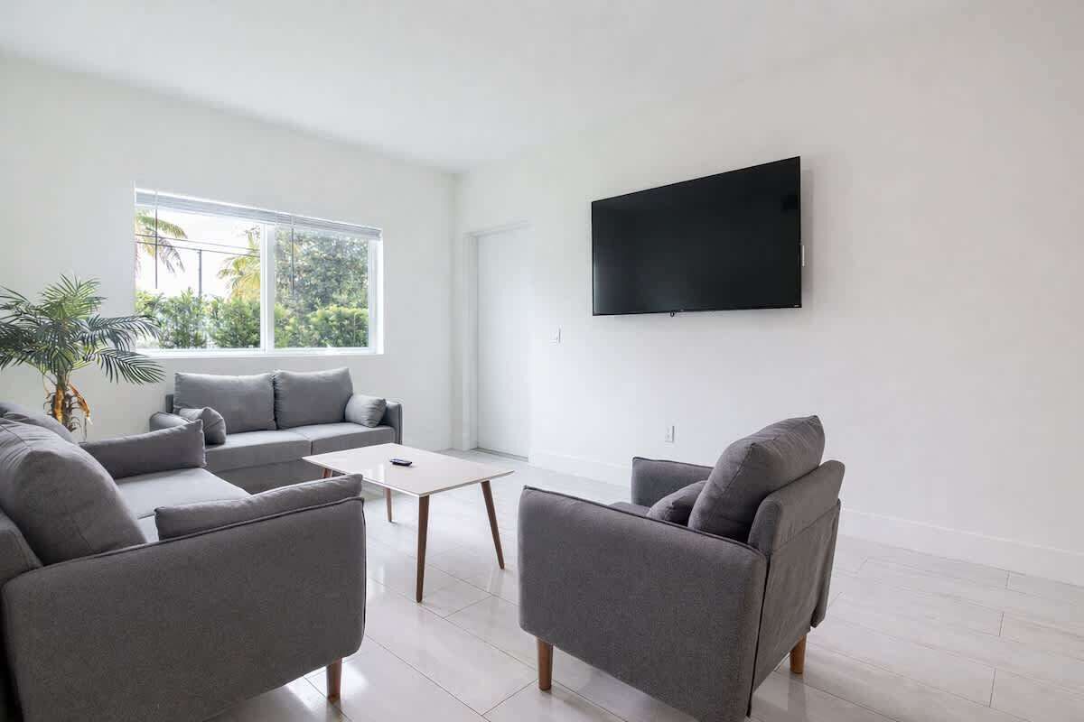 A modern living room with a grey sofa set, a coffee table, and a flat-screen TV mounted on the wall.