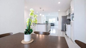 A modern kitchen with white cabinets, a dining table with a potted orchid, and a view into the living area.