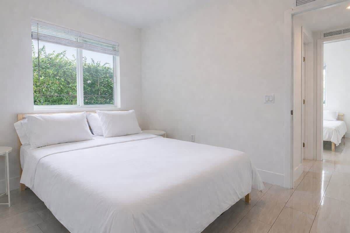 Une chambre spacieuse avec un grand lit, une table de chevet et une fenêtre équipée de stores.