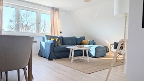 A modern living room with a blue sofa, a small white table, and a wicker chair. - Berth 5 - close to the beach and modern (Timmendorfer Strand)
