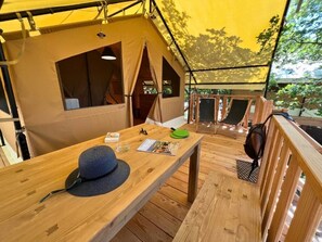 A tented accommodation with a wooden deck, a table with a hat and a magazine, and a view of the outdoors. - ZEcamping 3 étoiles animé piscine chauffée locatif 20m2 5 pers (Saint-Saturnin-lès-Apt)