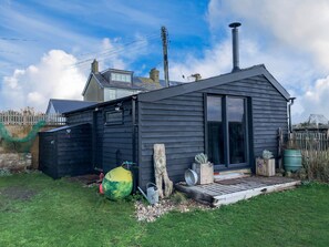 Eine moderne, dunkelholzene Holzhütte mit einem großen Schiebeglastür, einem Schornstein und einer kleinen Holzterrasse.