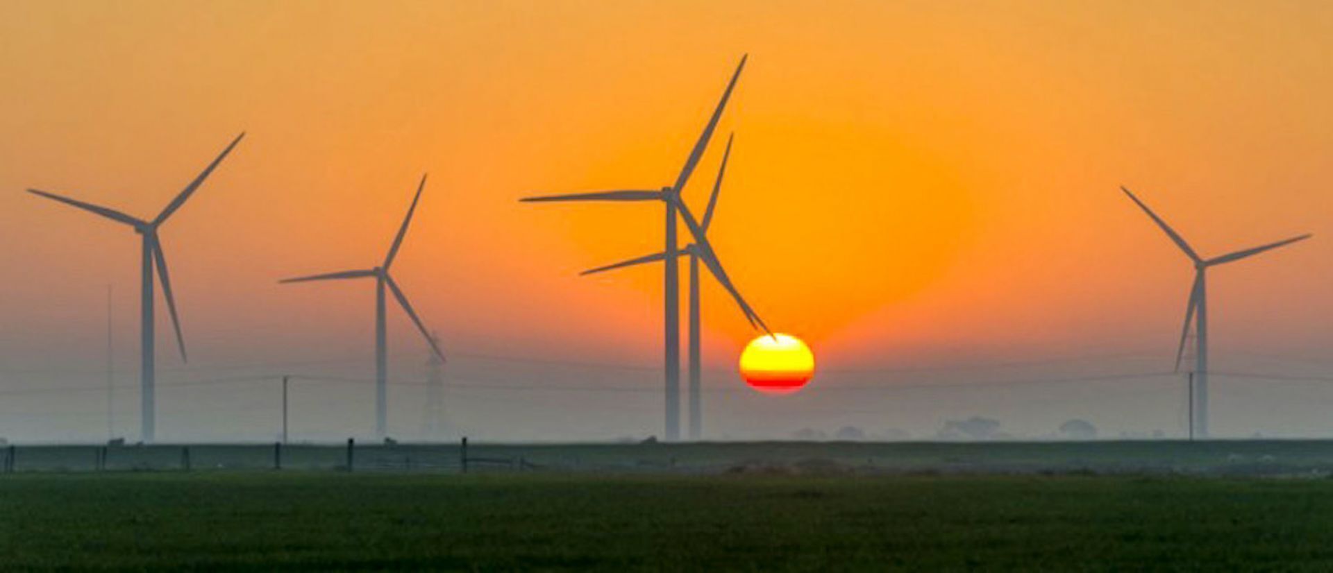 Un paysage avec des éoliennes et un soleil couchant.