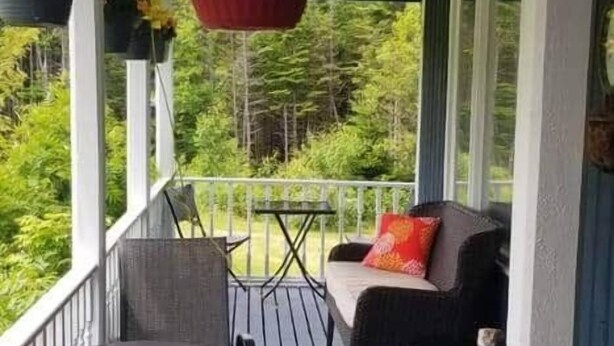 A porch with a white railing, a black outdoor chair, a small round table, and a hanging planter with green foliage. - The Garden Room, Trinity Guest House (Trinity)