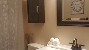 A bathroom with a toilet, a sink with a mirror above it, and a cabinet below the mirror. - The Garden Room, Trinity Guest House (Trinity)