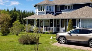 A two-story house with a covered porch and a car parked in the driveway. - The Garden Room, Trinity Guest House (Trinity)