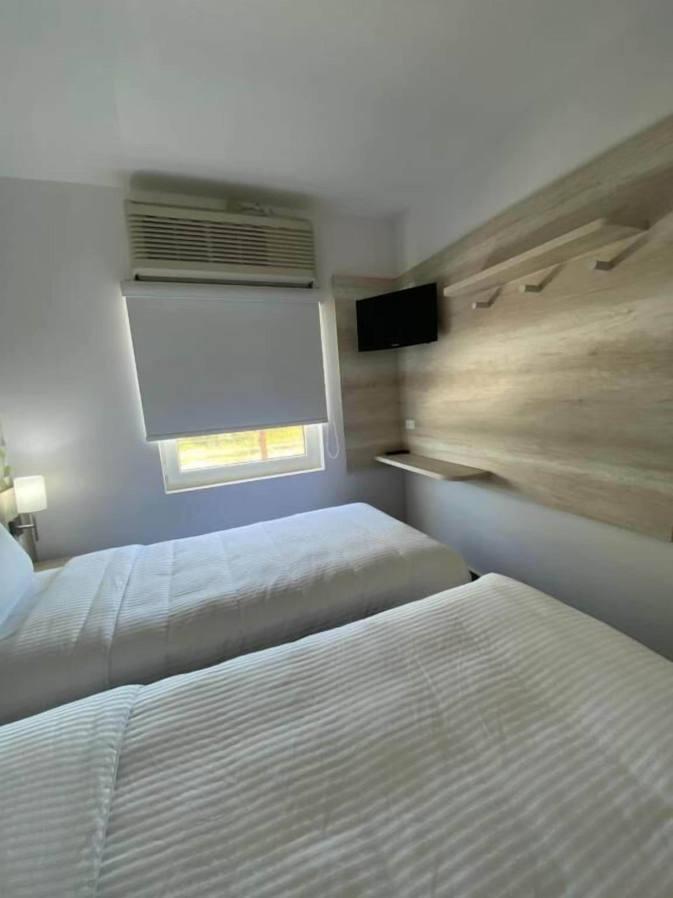 Un dormitorio con dos camas, un televisor montado en la pared y una ventana con persianas.