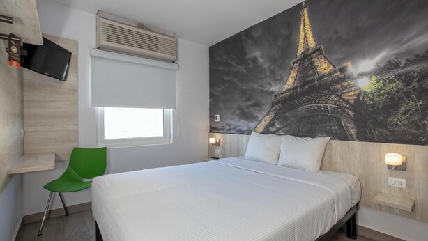 A hotel room with a large bed, a green chair, a flat-screen TV, an air conditioning unit, and a mural of the Eiffel Tower. - HI MONTERREY AEROPUERTO (Apodaca)