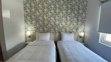 Habitación de hotel con dos camas, un diseño de pared geométrico, lámparas de noche y una ventana con persianas.