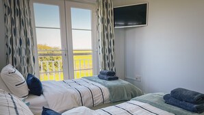 Ein Hotelzimmer mit zwei Betten, einem an der Wand befestigten Fernseher und einem Balkon mit Blick auf die Landschaft.