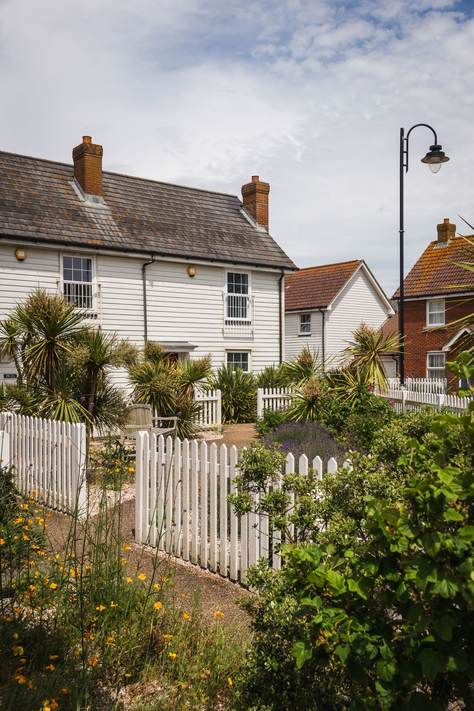 A white two-story house with a white picket fence, surrounded by greenery and yellow flowers.