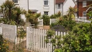 Uma casa branca de dois andares com cerca branca de piquete, cercada por vegetação e flores amarelas.