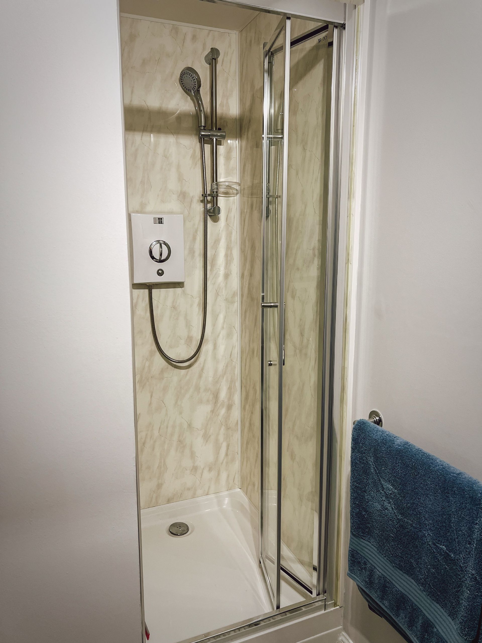A glass-enclosed shower stall with a handheld showerhead and a wall-mounted control panel.