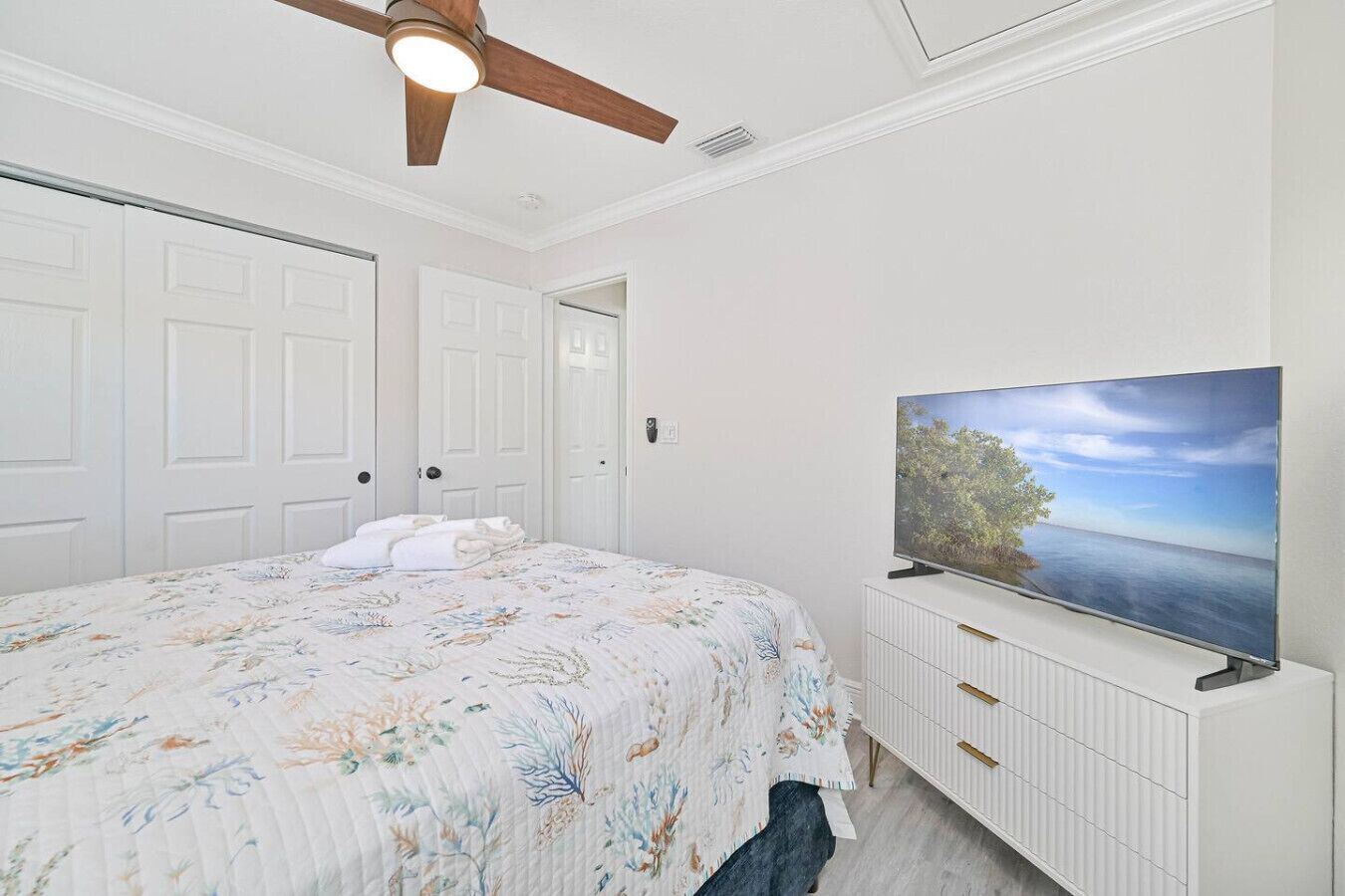 Un dormitorio con cama, ventilador de techo, televisor y puertas blancas.