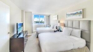 Habitación de hotel con dos camas, televisión, escritorio y ventana con vistas a la ciudad.